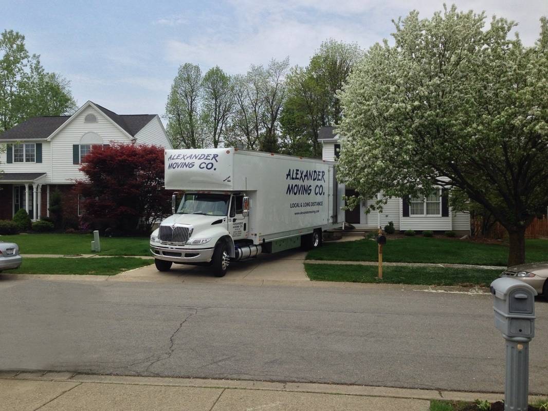A big white truck with Alexander moving co. written on it parked in front of house